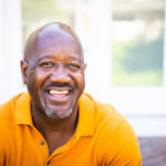Home a mature black man looks out while standing on his porch